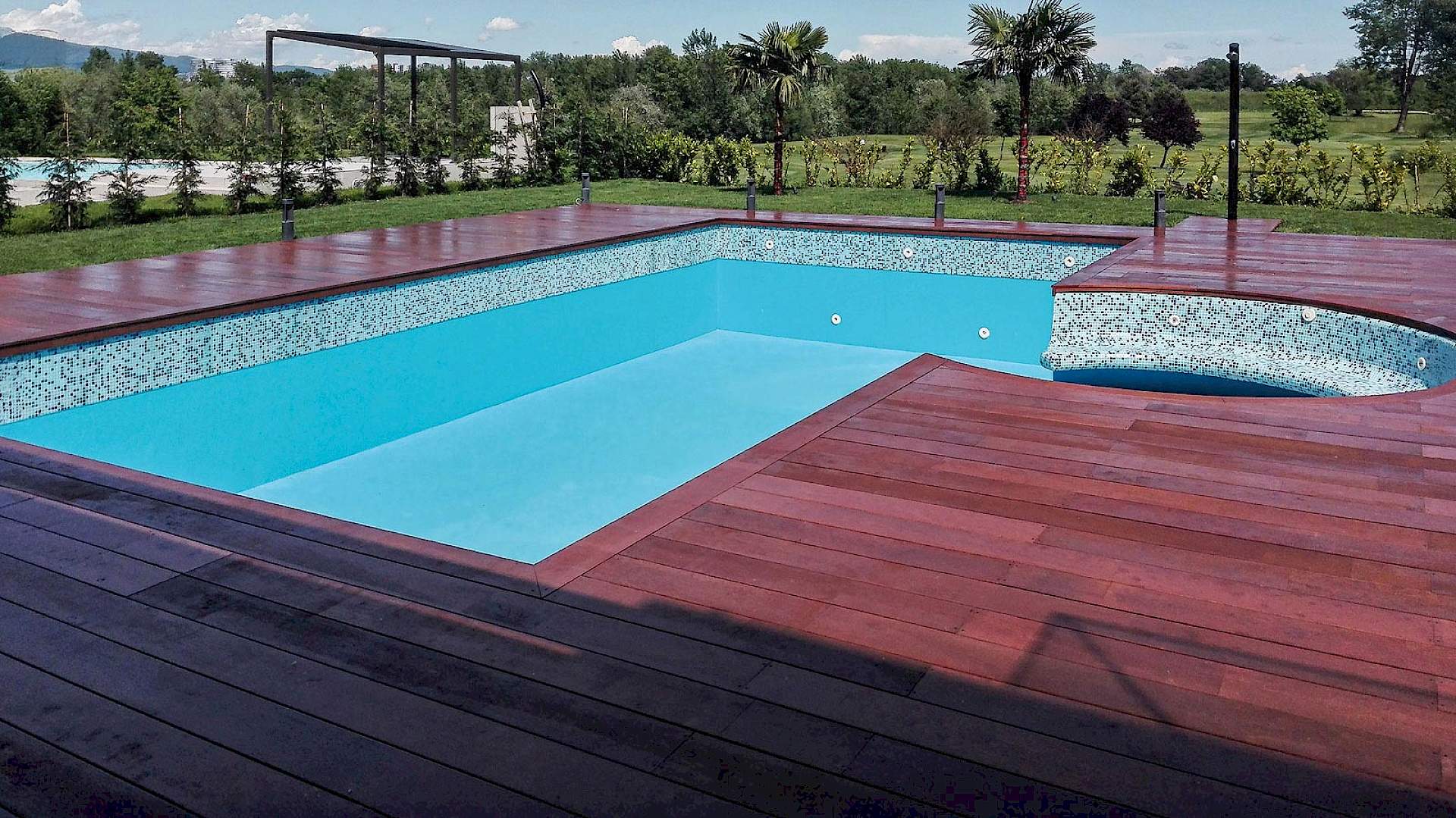 Izgrađen vanjski bazen nepravilnog oblika s detaljima od mozaika i drvenom terasom (decking) za kuću za odmor.