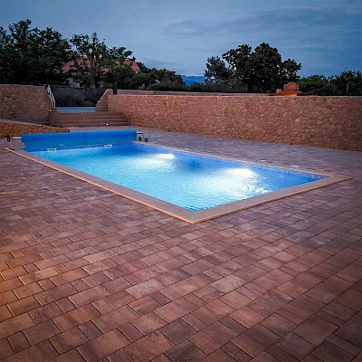 Noćni prikaz osvijetljenog bazena s ugrađenom LED rasvjetom, rolo prekrivačem i kamenim opločenjem