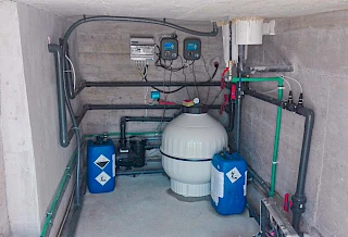 Precizna ugradnja bazenske tehnike u podzemnoj betonskoj strojarnici s velikim bijelim filterom, zidnom automatikom i plavim kanistrima za doziranje