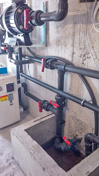 Precizna montaža velike zidne pumpe za bazen s debelim PVC cijevima i crvenim ventilima unutar betonske strojarnice