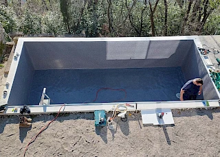 Pogled odozgo na majstora koji postavlja modernu sivu armiranu foliju u pravokutnu betonsku školjku vanjskog bazena