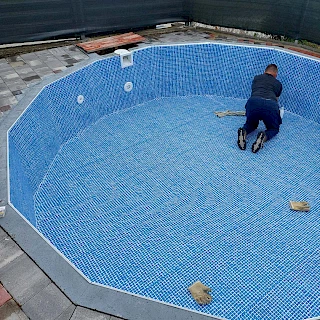 Majstor precizno postavlja armiranu bazensku foliju s uzorkom plavog mozaika u betonski bazen višekutnog, nestandardnog oblika