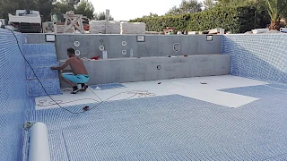 Radnik postavlja protukliznu bazensku foliju s uzorkom plavog mozaika na stepenice tijekom ugradnje u praznu školjku bazena