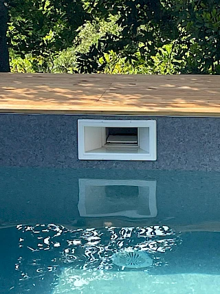 Detalj napunjenog modernog bazena sa sivom armiranom folijom, bijelim ugradbenim skimmerom i drvenom terasom na rubu.