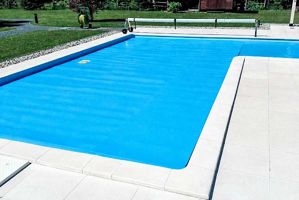 Vanjski bazen preko kojeg je razvučen plavi ljetni solarni prekrivač za bazene s namatalicom u pozadini