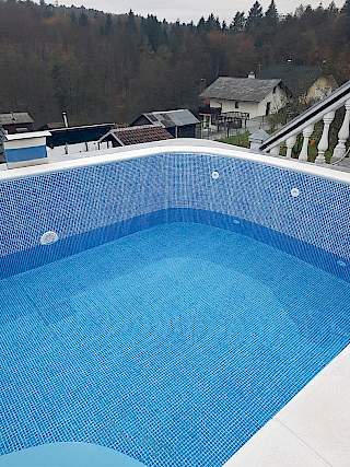 Vanjski bazen s ugrađenom plavom mozaik folijom i bijelim rubnim kamenom, s pogledom na šumu i kuće u Gorskom kotaru