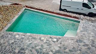 Pogled odozgo na napunjen vanjski bazen okružen kamenim pločama, gdje postavljena folija stvara jasan tirkizni efekt vode