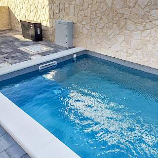 Prikaz ugrađene moderne crne inverter toplinske pumpe za grijanje bazena, smještene uz kameni zid pored vanjskog bazena.