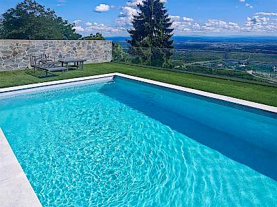 Moderni vanjski bazen s tirkiznom vodom, zelenim travnjakom i panoramskim pogledom na brežuljke