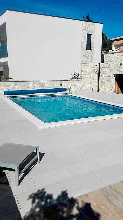 Vanjski bazen s tirkiznom vodom i rolo sustavom za ljetni prekrivač ispred moderne kamene kuće u Staroj Novalji
