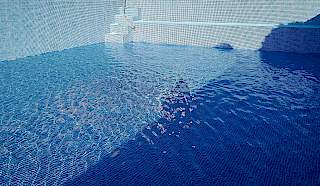 Proces prvog punjenja bazena čistom vodom preko svježe ugrađene plave mozaik folije, s vidljivim odsjajem na površini